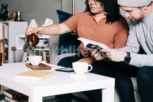 Woman Pouring a Cup of Coffee While Man Reads a Book