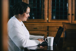 Woman Working on a Laptop with a Cup of Coffee at the Table  image 1