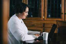 Woman Working on a Laptop with a Cup of Coffee at the Table  image 3