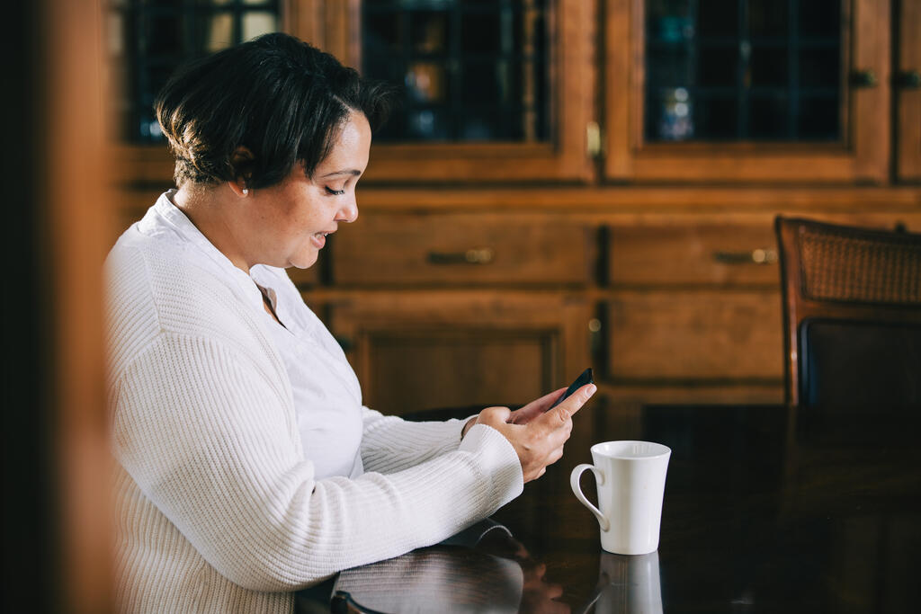 Woman Looking at Her Phone with a Cup of Coffee at the Table large preview