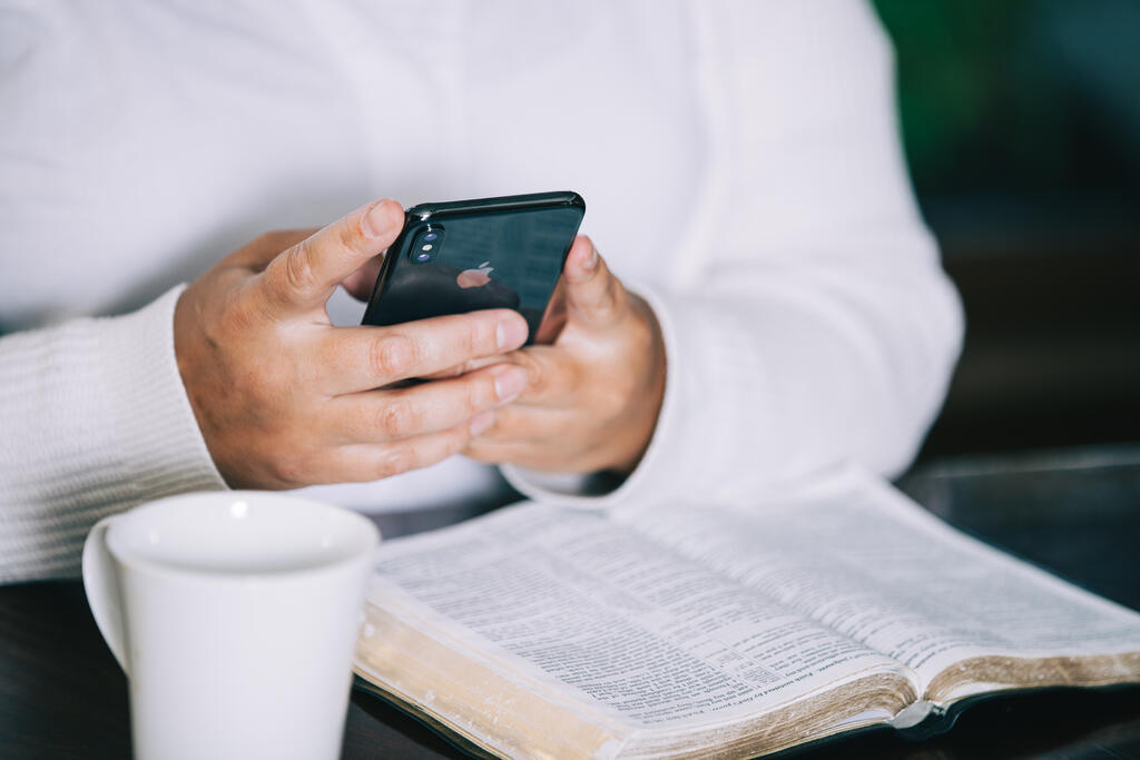 Woman Holding Her Phone with an Open Bible and a Cup of Coffee large preview