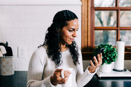 Woman Looking at Her Phone with a Cup of Coffee in the Kitchen  image 2