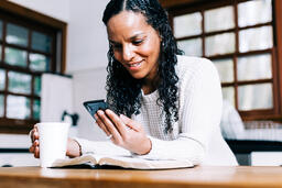 Woman Looking at Her Phone with an Open Bible and Cup of Coffee  image 2