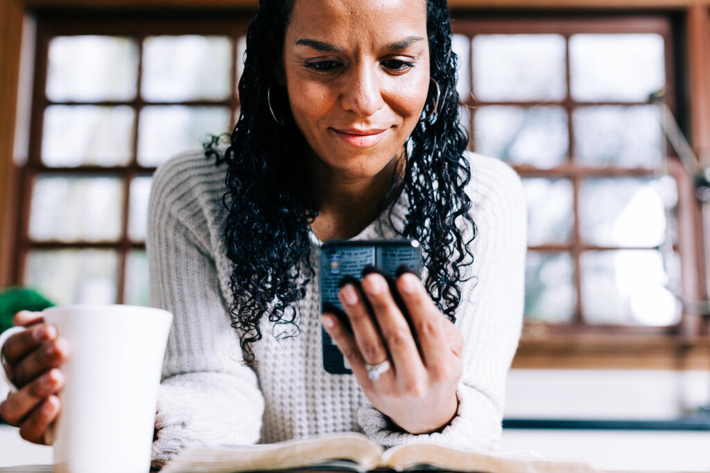 Woman Looking at Her Phone with an Open Bible and Cup of Coffee large preview