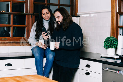 Husband and Wife Looking at a Phone with Cups of Coffee in the Kitchen