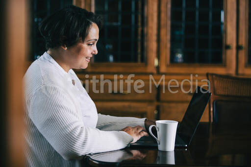 Woman Working on a Laptop with a Cup of Coffee at the Table