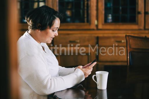 Woman Looking at Her Phone with a Cup of Coffee at the Table