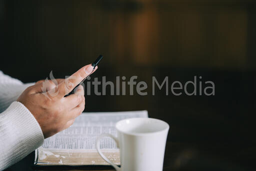 Woman Holding Her Phone with an Open Bible and a Cup of Coffee