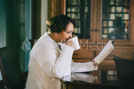 Woman Reading the Bible and Drinking Coffee at a Table