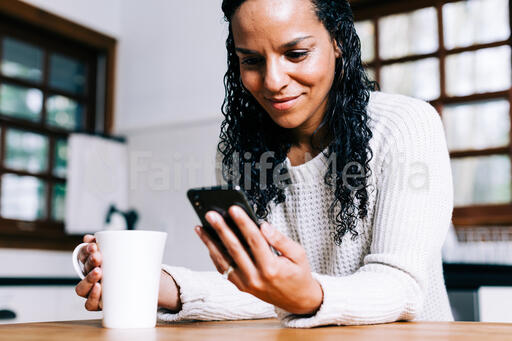 Woman Looking at Her Phone with a Cup of Coffee in the Kitchen