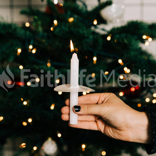 Hand in Frame Holding a Candle in Front of the Christmas Tree