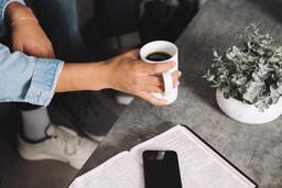 Man Picking up Cup of Coffee Next to Open Bible and Smart Phone  image 2