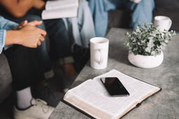 Man Picking up Cup of Coffee Next to Open Bible and Smart Phone  image 1