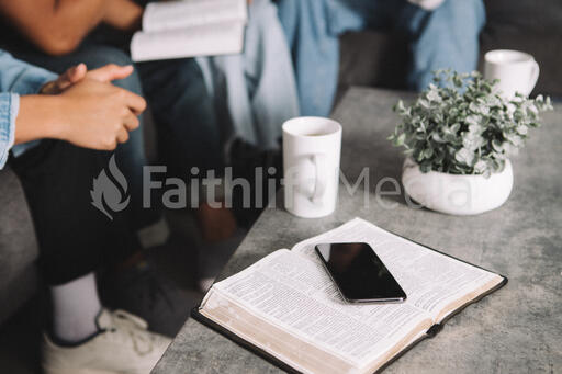 Man Picking up Cup of Coffee Next to Open Bible and Smart Phone