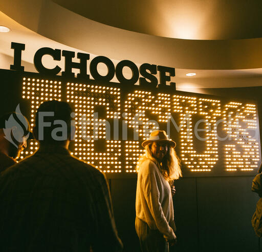 Woman Walking In Front of Lit Up I Choose Jesus Sign