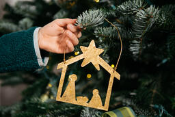 Young Girl's Hand Hanging a Nativity Scene Christmas Ornament on the Tree  image 2