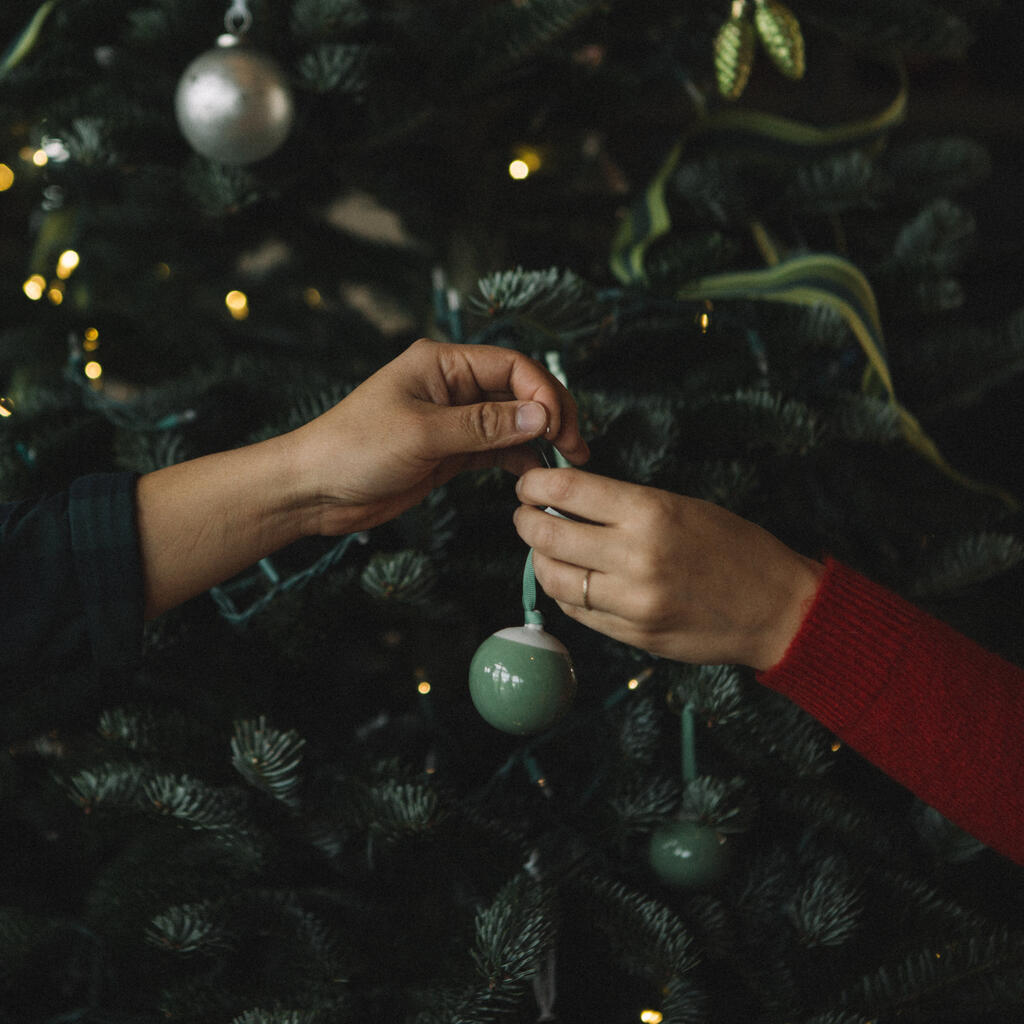Hands Sharing a Christmas Ornament in Front of the Tree large preview