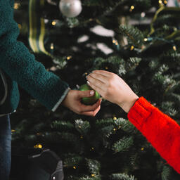 Kids' Hands Sharing Christmas Ornaments in Front of the Tree  image 1