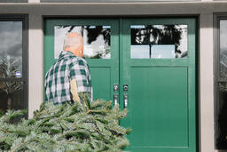 Man with Gray Hair Carrying a Christmas Tree into the House  image 1