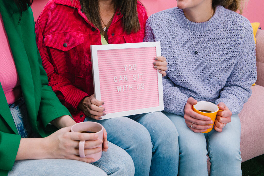 Women Holding a Pink Letter Board Reading YOU CAN SIT WITH US large preview