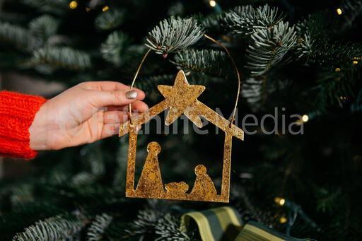 Young Girl's Hand Hanging a Nativity Scene Christmas Ornament on the Tree