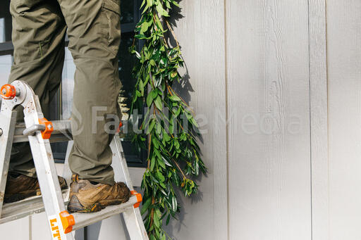 Man on a Ladder Putting Up Christmas Garland