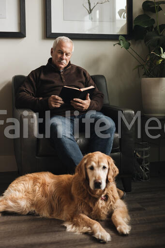 Senior Man Reading the Bible at Home with His Dog