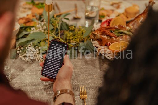 Man Reading from the Bible on His Phone before Thanksgiving Dinner