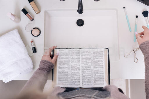 Woman Reading the Bible While Doing Her Make-Up