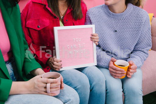 Women Holding a Pink Letter Board Reading YOU CAN SIT WITH US